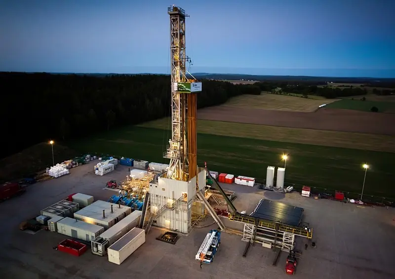 A land drilling rig lit at dusk on flat farmland, seen from the air