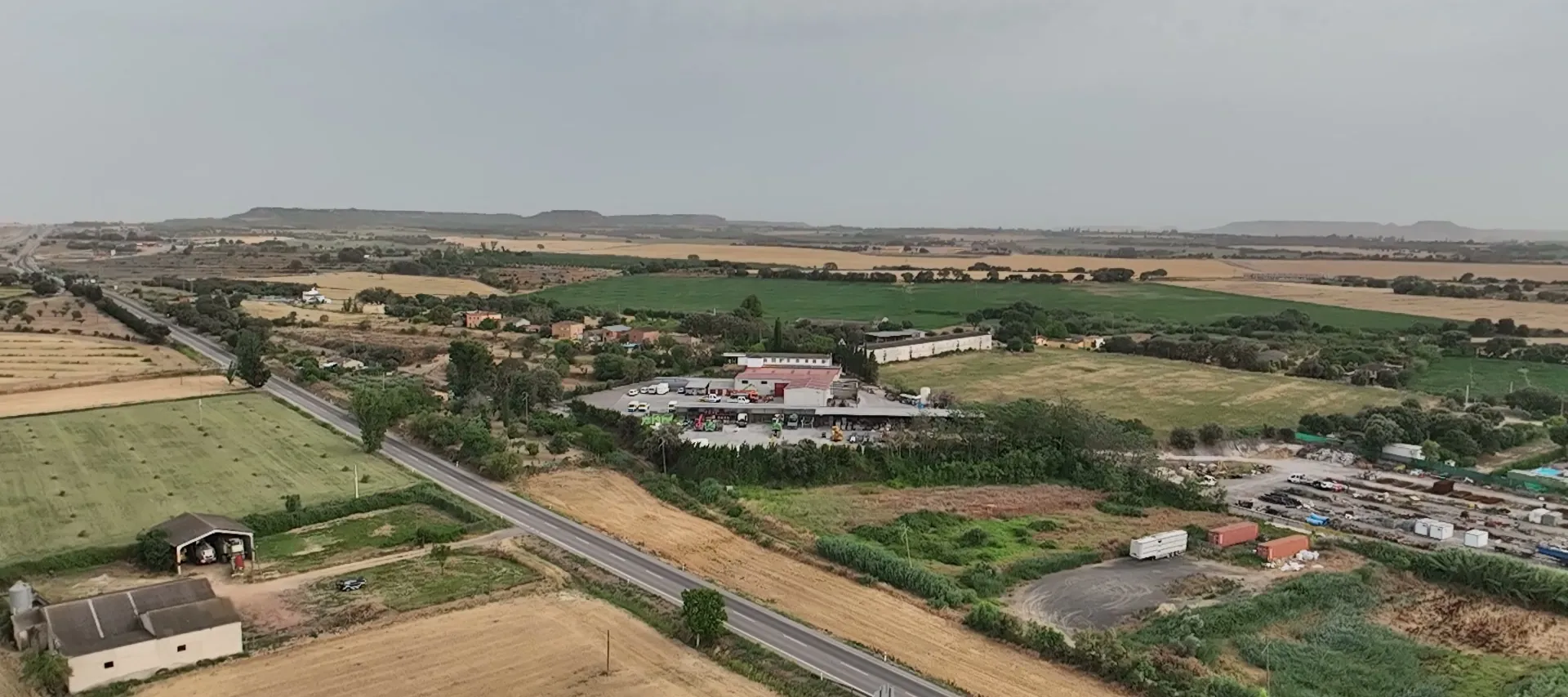 Flat farmland, a road and farm buildings near Monzón, low mesas on the horizon